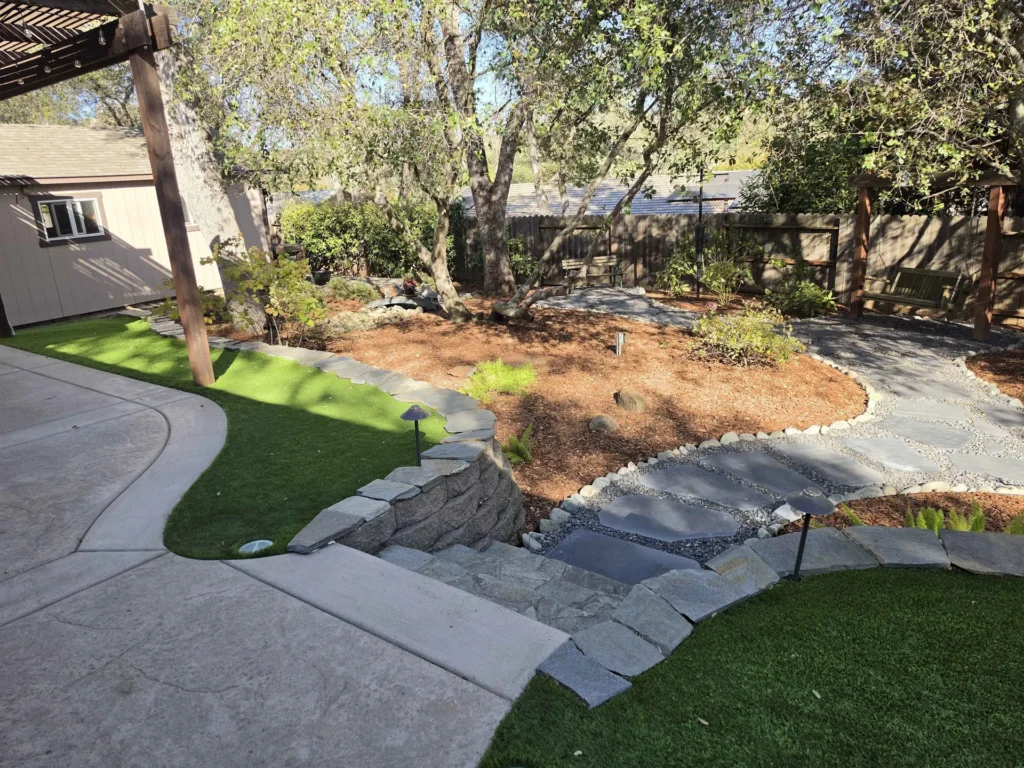 Stone steps and a curved flagstone path beside turf and mulched planting beds.
