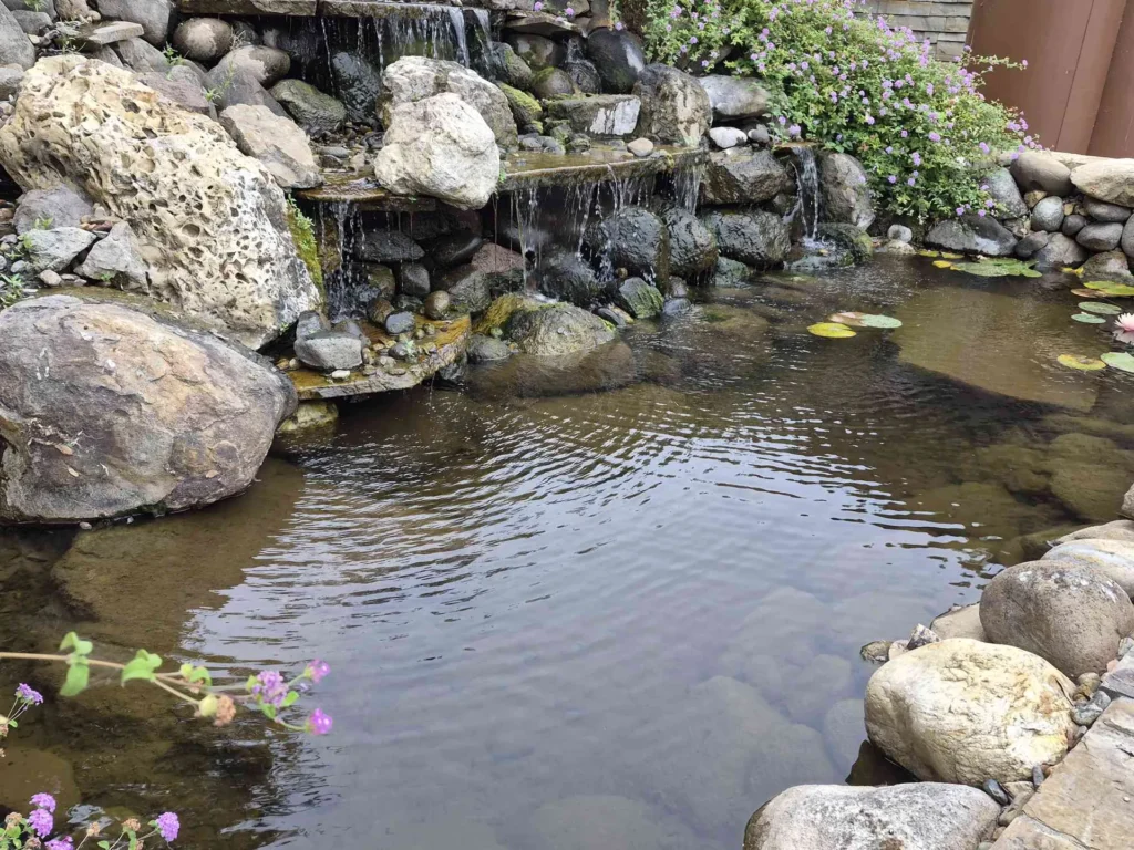 Water cascading over stacked rocks into a garden pond with lily pads.