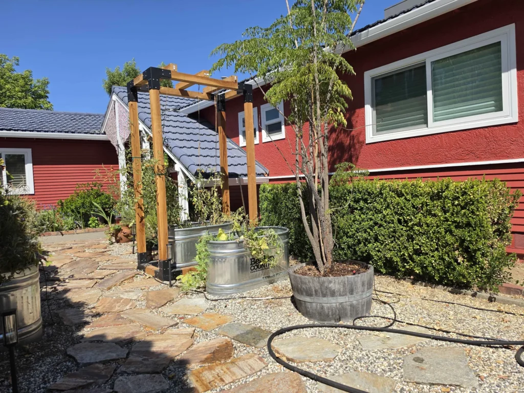 A wood garden arbor with planters beside a flagstone path and clipped hedge.
