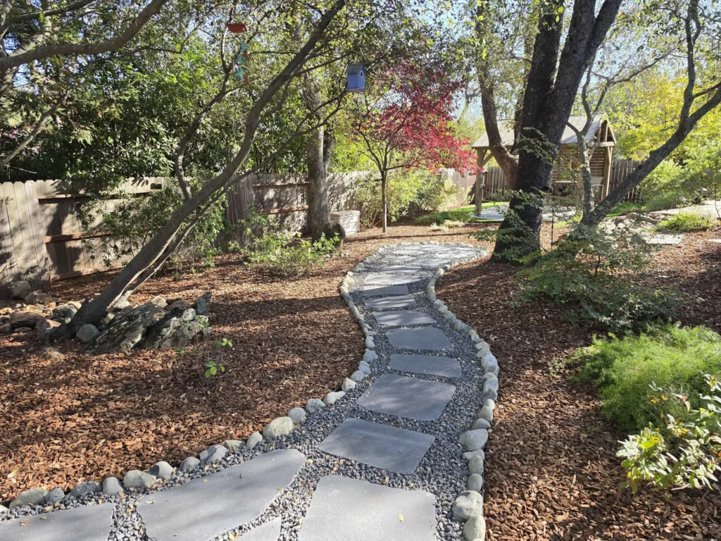 A curving flagstone path with gravel joints and stone edging through a mulched garden.